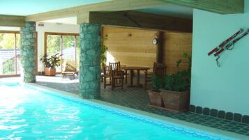 Una piscina interior con pilares de piedra, muebles de madera y un reloj en la pared.
