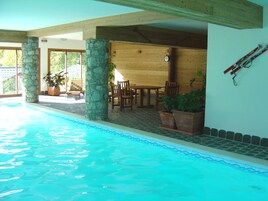 An indoor swimming pool with stone pillars, wooden furniture, and a clock on the wall.