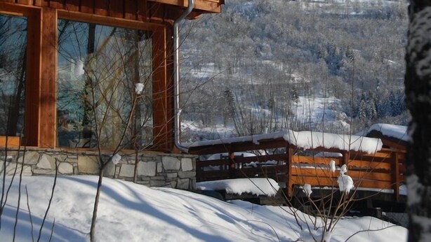 A wooden cabin with a snow-covered roof, stone foundation, and large windows. - Hôtel l'Autantic (Bourg-Saint-Maurice)