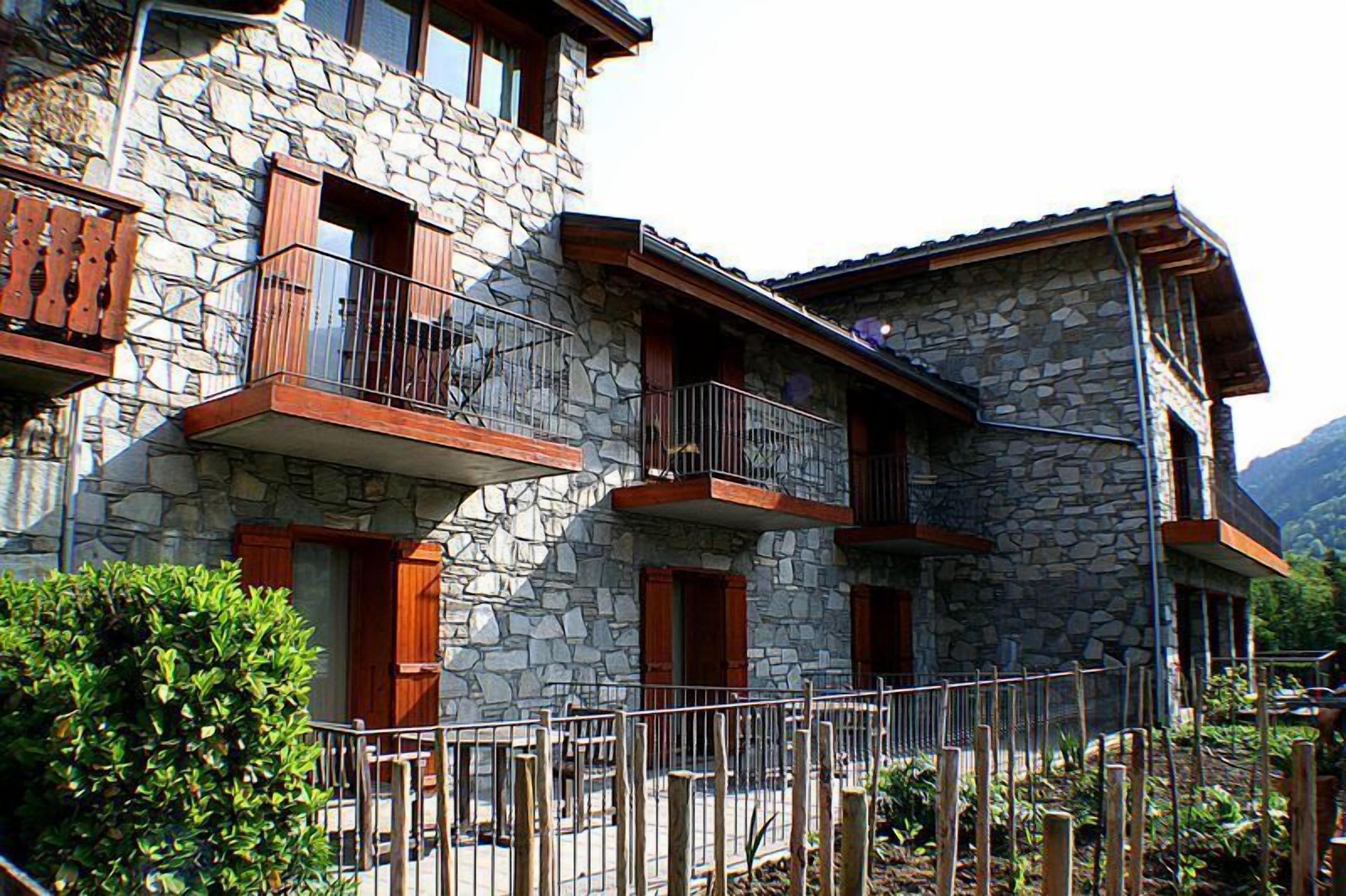 Un bâtiment en pierre doté de balcons, de volets en bois et d’une clôture en métal.