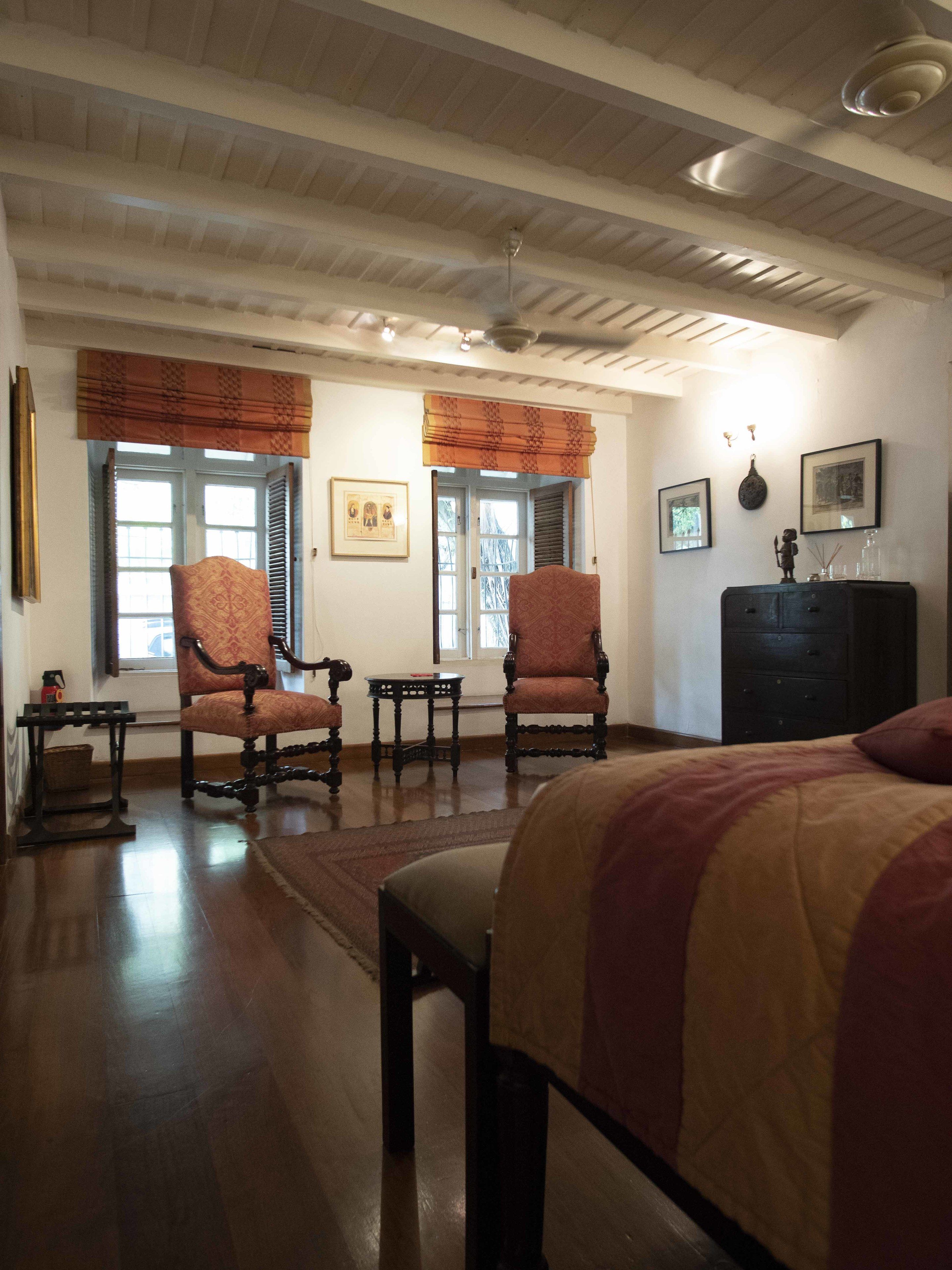A spacious room with a large bed, two armchairs, a small table, and a dresser.