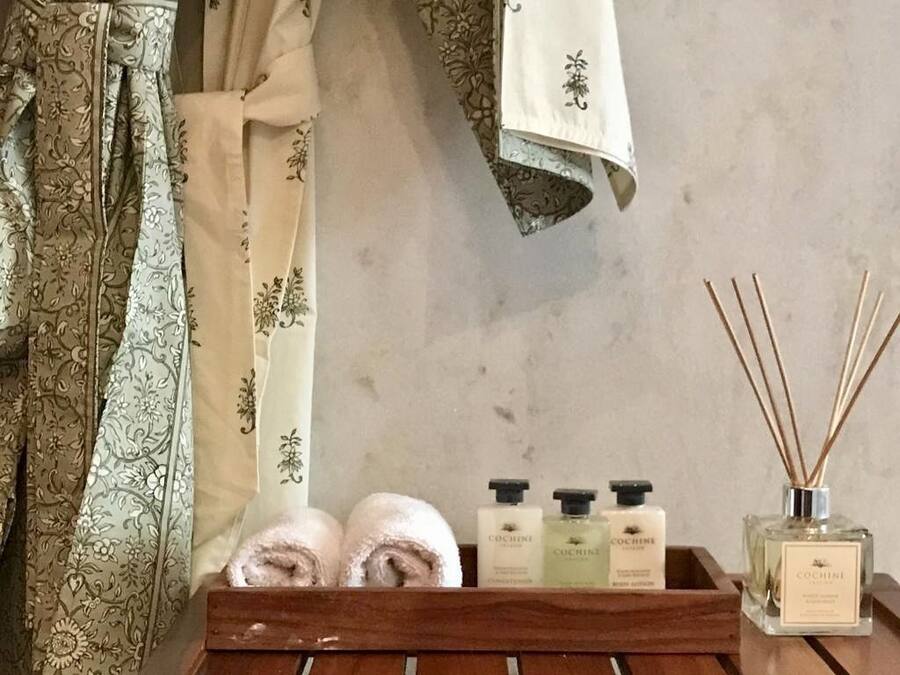 Een badkamer met een houten dienblad waarop twee handdoeken, drie flesjes COCINE douchegel en een rietverspreider liggen.