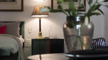 Una habitación de hotel con una cama, una mesita de noche con una lámpara, un jarrón con plantas y cuadros en la pared.