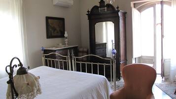 Un dormitorio con cama, una silla, tocador, espejo y candelabro.