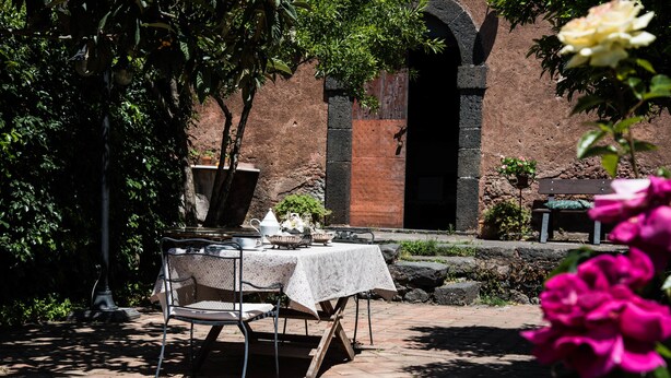 Un patio al aire libre con una mesa preparada para dos personas, rodeado de follaje y un muro de ladrillo.