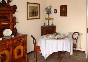 A dining room with a round table set for four, surrounded by wooden chairs. A vintage wooden cabinet with a mirror and a framed picture hangs on the wall.