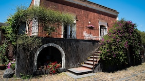 Un edificio histórico con un arco de piedra en la entrada, un balcón con barandilla de hierro forjado y una escalera que conduce al piso superior.