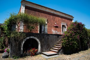 Un edificio histórico con un arco de piedra en la entrada, un balcón con barandilla de hierro forjado y una escalera que conduce al piso superior.