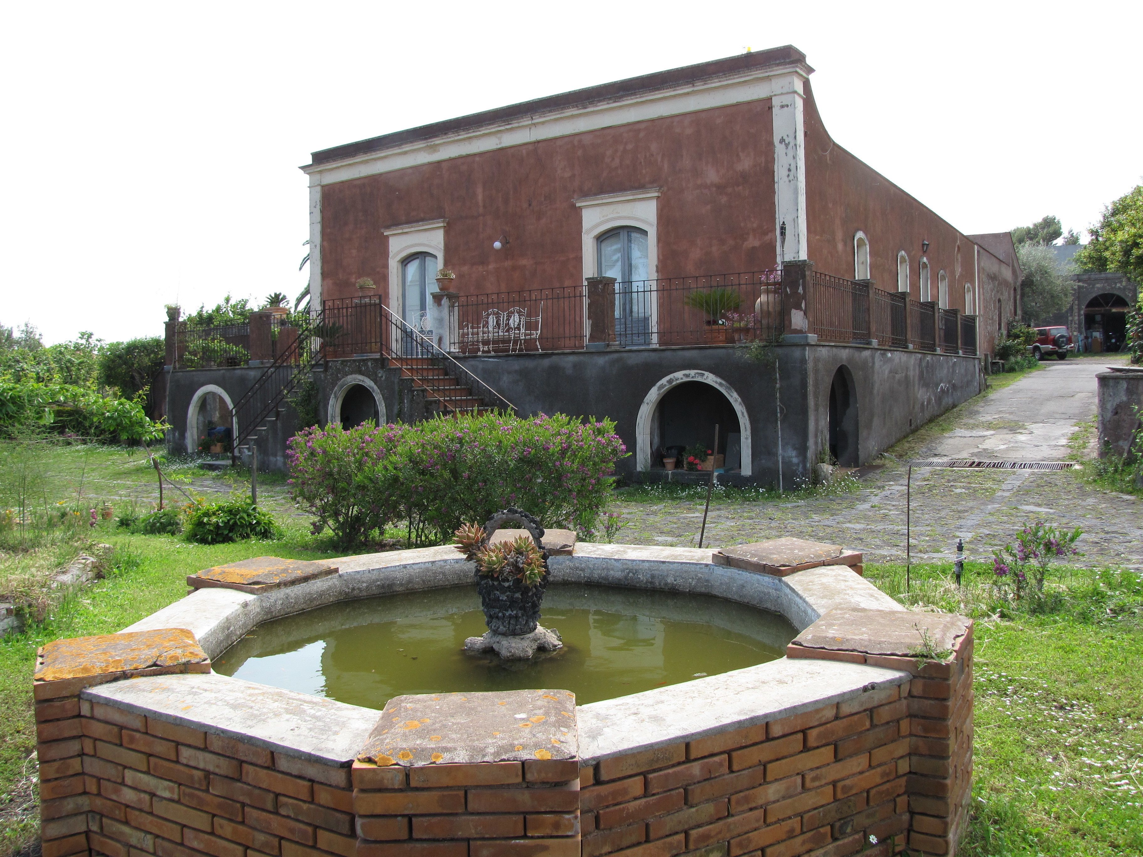 Ein Gebäude mit Ziegelverkleidung, einem Springbrunnen im Vordergrund und einem gepflasterten Weg zum Eingang.