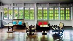 Una habitación con ventanas amplias, un sofá con cojines, una mesita y una silla.
