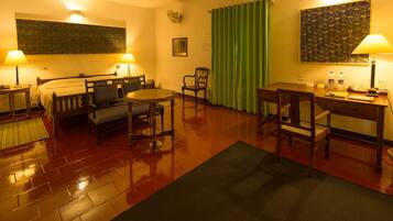 A hotel room with a bed, two chairs, a small table, a desk, and a green curtain.