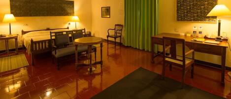 A hotel room with a bed, two chairs, a small table, a desk, and a green curtain.