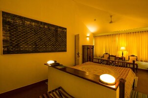 Quarto de hotel com cama, escrivaninha, cadeira, luminária e um quadro na parede.