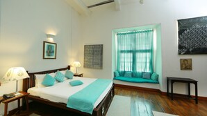 Un dormitorio con cama, lámparas de noche, una ventana con cortinas, un sofá y obras de arte en las paredes.