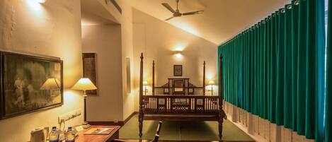 A hotel room with a wooden bed, a desk with a chair, a lamp, and a painting on the wall.