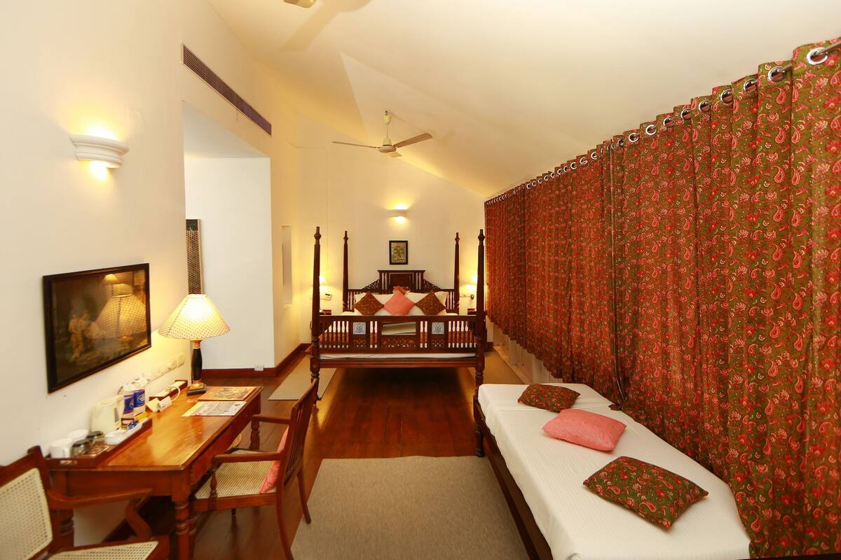 A hotel room with a bed, a desk, a chair, a ceiling fan, and a window with curtains.