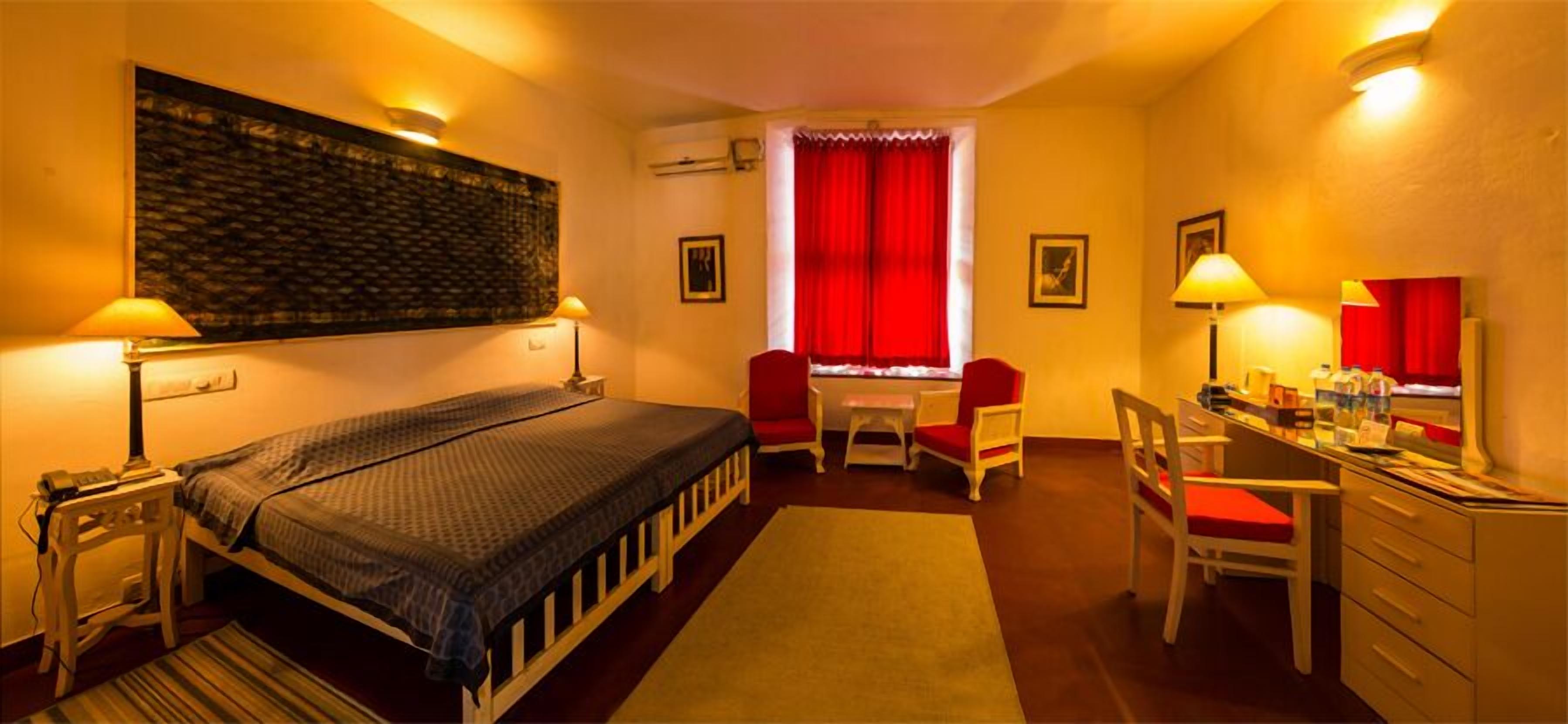 Ett hotellrum med en säng, ett skrivbord, en stol och en röd gardin.