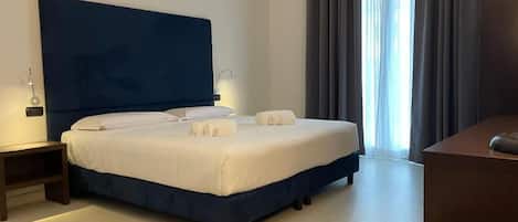 A modern hotel room with a large bed, a desk, and a view of the outdoors.