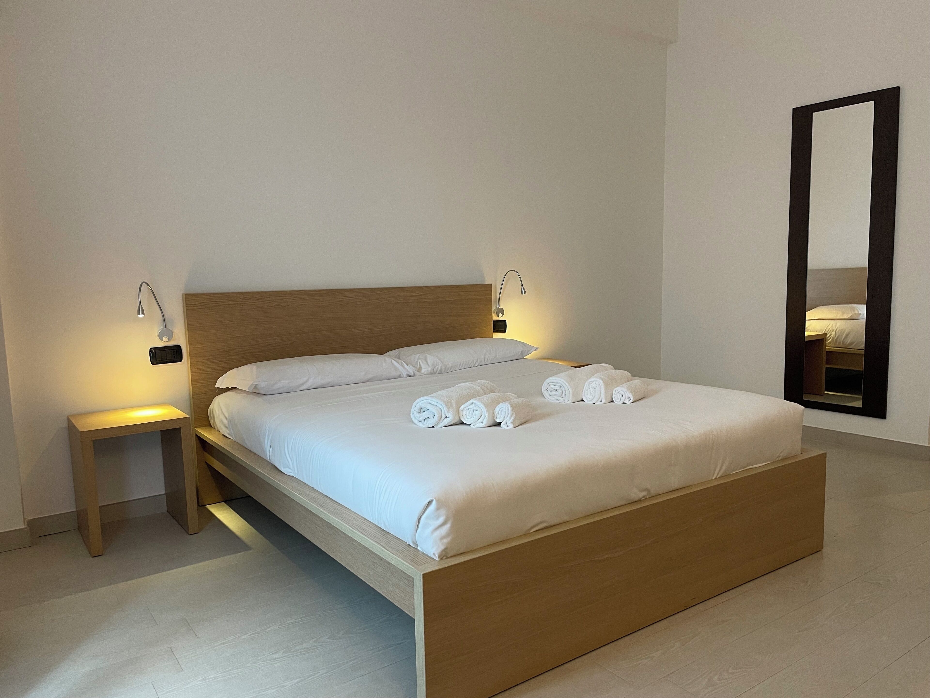 Ein modernes Hotelzimmer mit einem hölzernen Bett, weißen Bettwäsche und einem Nachttisch mit Lampe.