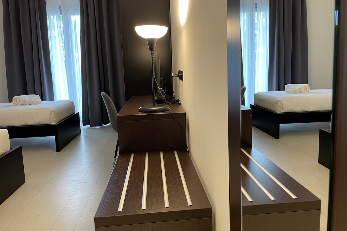 A hotel room with two beds, a desk, a chair, a lamp, and a large mirror.