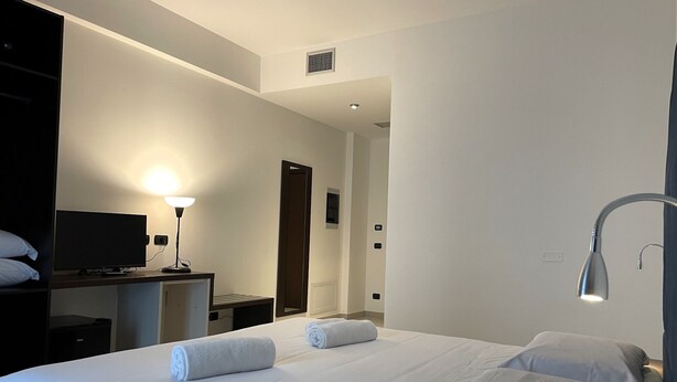 A hotel room with a large bed, a desk with a computer, a lamp, and a door leading to another room. - Maestrale Resort Hotel - Alberese, Grosseto (Grosseto)