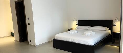 Un dormitorio moderno con estructura de cama negra, ropa de cama blanca y dos lámparas de noche.