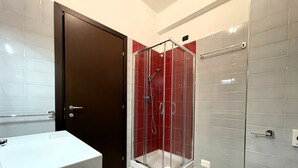 A bathroom with a white sink, a toilet, and a glass-enclosed shower with red tiles. - Maestrale Resort Hotel - Alberese, Grosseto (Grosseto)