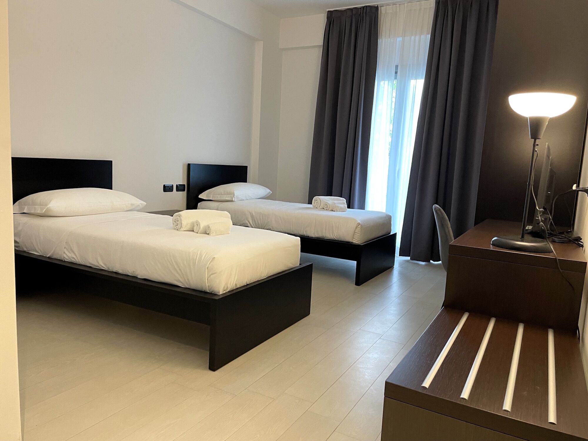 A hotel room with two beds, a desk with a computer, and a lamp.