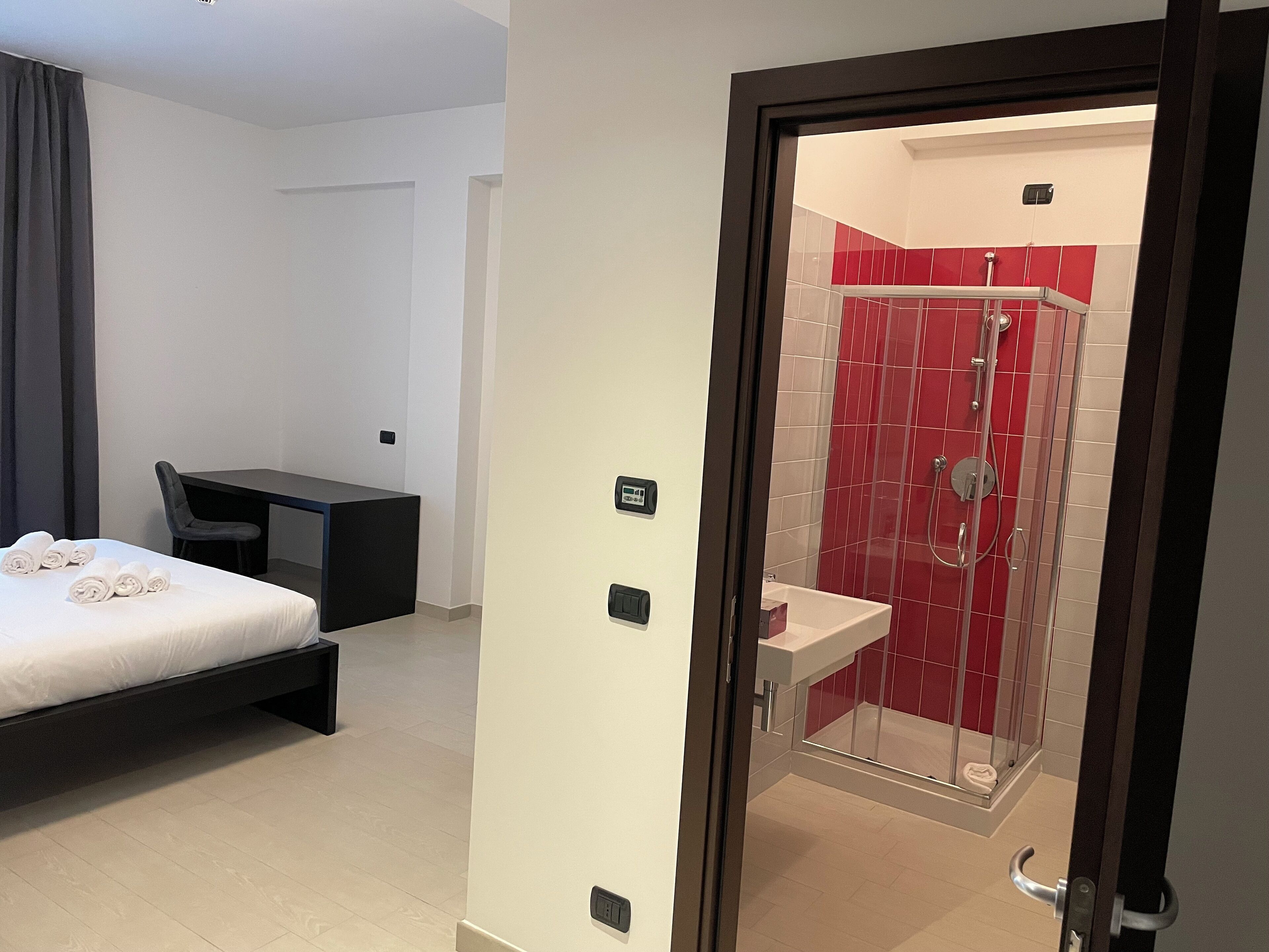 A hotel room with a bed, a desk, a chair, and a bathroom with a shower and sink.