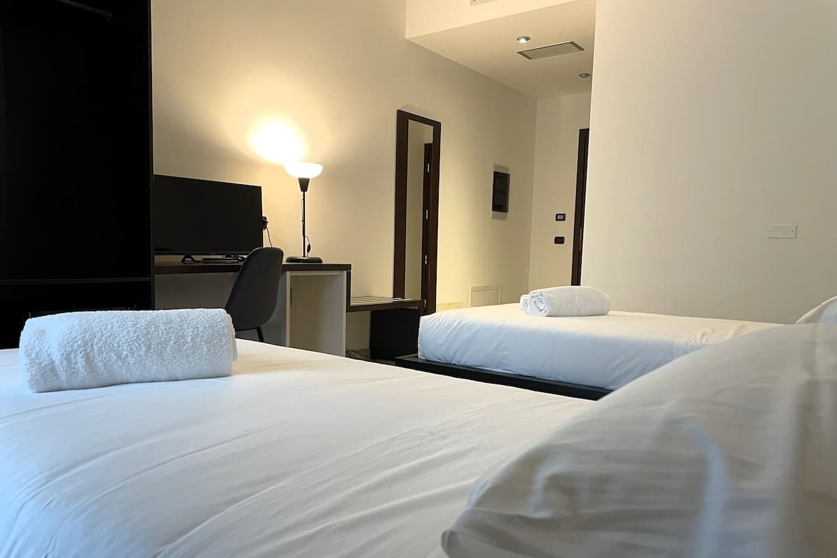 A hotel room with two beds, a desk, a chair, a TV, and a lamp.