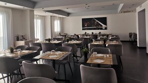 A modern hotel dining area with multiple tables and chairs, a cityscape view, and a large painting on the wall. - Maestrale Resort Hotel - Alberese, Grosseto (Grosseto)