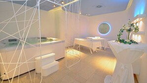 A modern spa room with a hot tub, a white chair, and a table with a floral arrangement. - Incontro Hotel & Spa (Ariano Irpino)