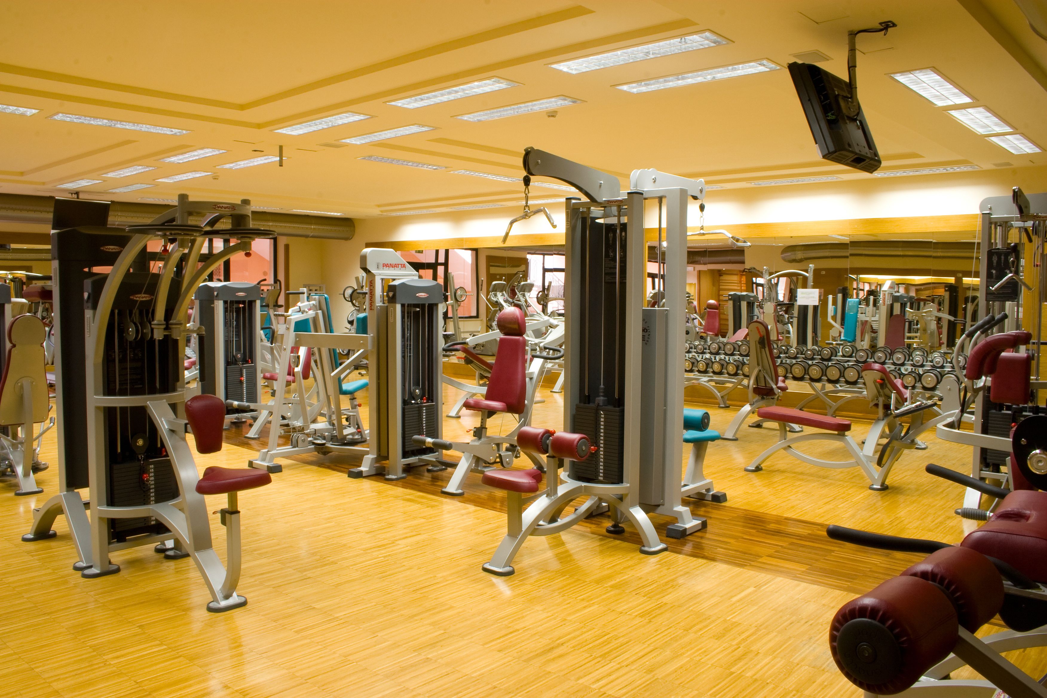 A gym with various exercise machines, wooden flooring, and a ceiling with recessed lighting.