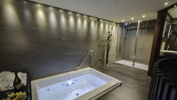 A modern bathroom with a large bathtub, a glass shower enclosure, and a dark wooden floor. - Incontro Hotel & Spa (Ariano Irpino)