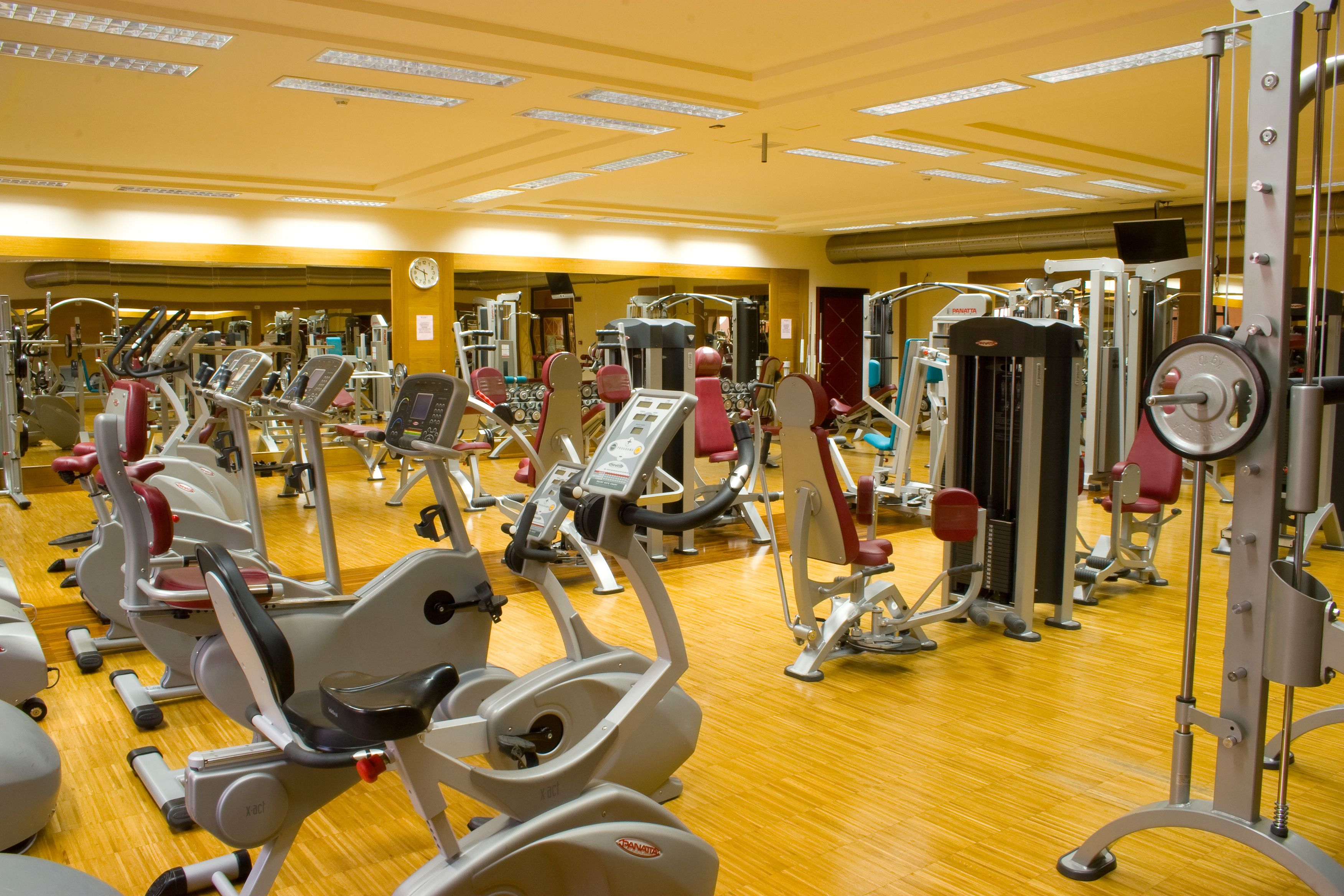 A gym with various exercise machines, wooden flooring, and a mirrored wall.