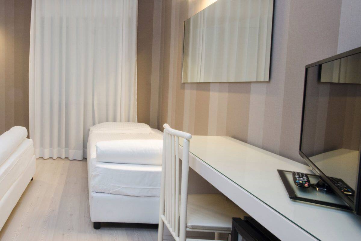 A hotel room with a bed, a desk with a computer, and a mirror.