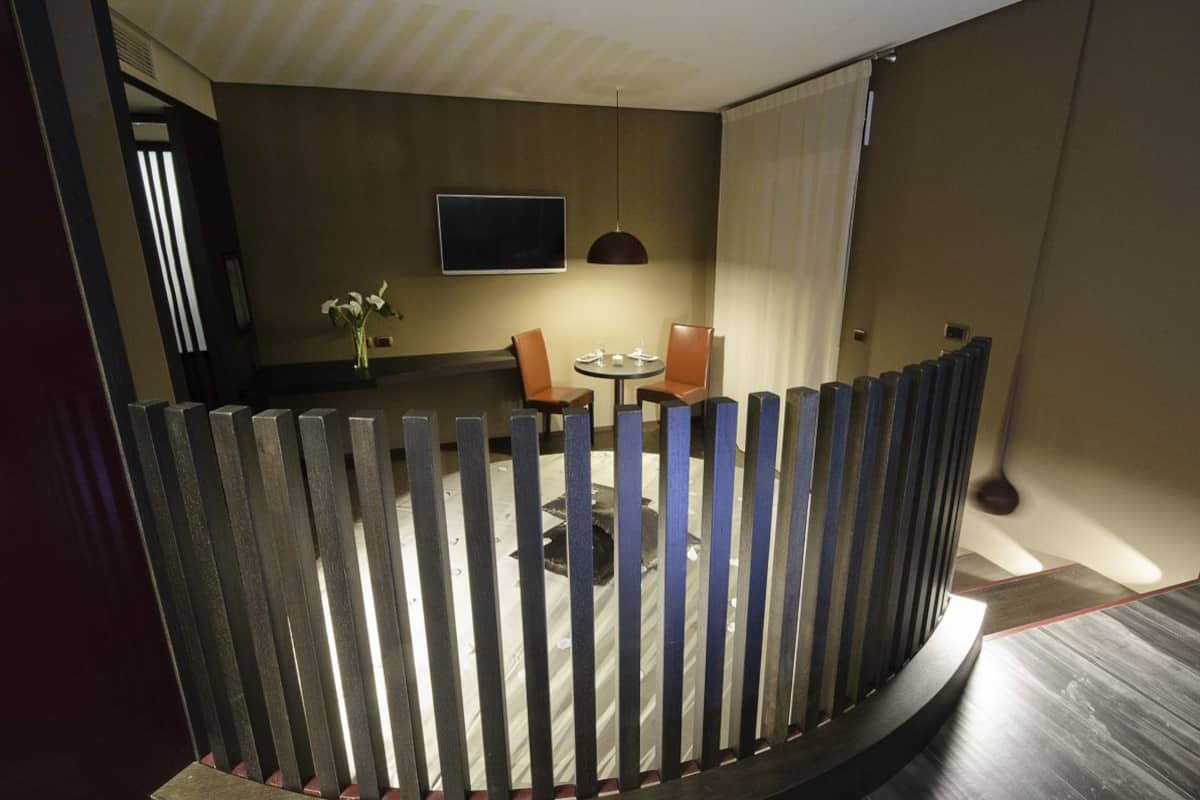 A hotel room with a balcony, a round table, two chairs, a TV, and a vase with flowers.