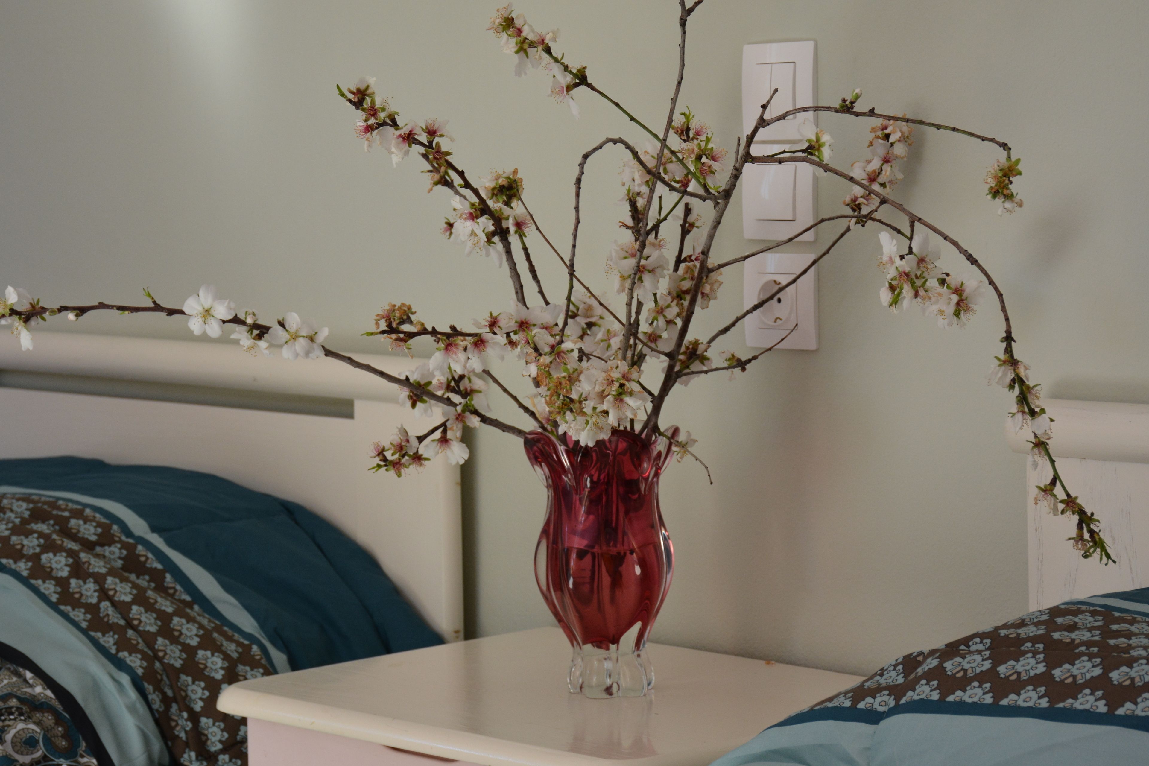 A vase with branches and flowers on a bedside table.