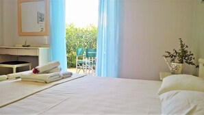 A hotel room with a bed, a desk, a chair, and a view of greenery outside. - Aloni Studios & Apartments (Kefalonia)