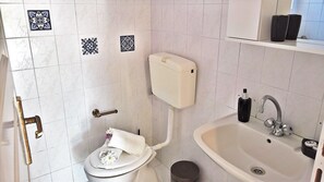 A bathroom with a toilet, sink, and a toilet paper holder. - Aloni Studios & Apartments (Kefalonia)
