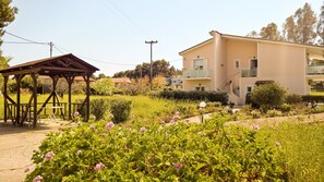 A two-story building with a balcony, surrounded by a garden with pink flowers. - Aloni Studios & Apartments (Kefalonia)