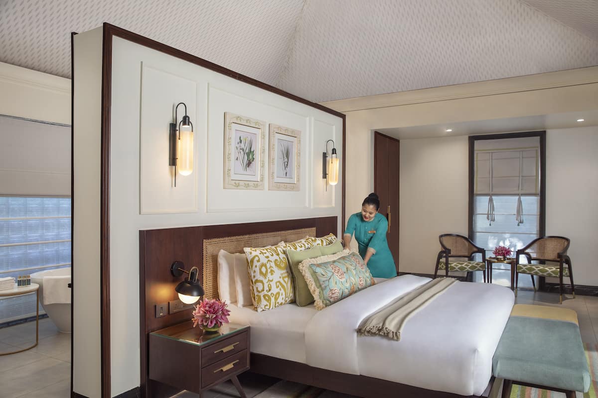 A well-appointed hotel room with a large bed, a nightstand with a lamp, a small table with a vase of flowers, and two chairs in the corner.