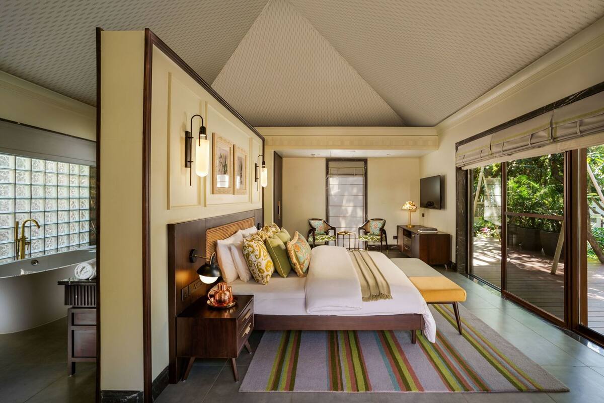 A hotel room with a large bed, a desk, a chair, a TV, and a view of the outdoors.