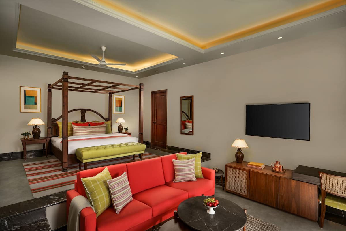 A hotel room with a four-poster bed, a red sofa, a coffee table, and a flat-screen TV.