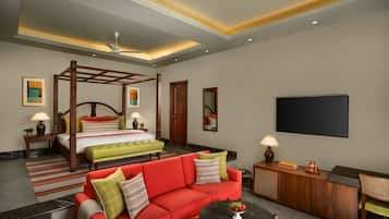A hotel room with a four-poster bed, a red sofa, a coffee table, and a flat-screen TV.