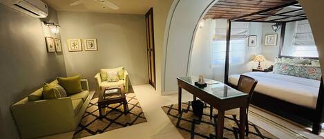 A hotel room with a sofa, armchair, dining table, and a bed.
