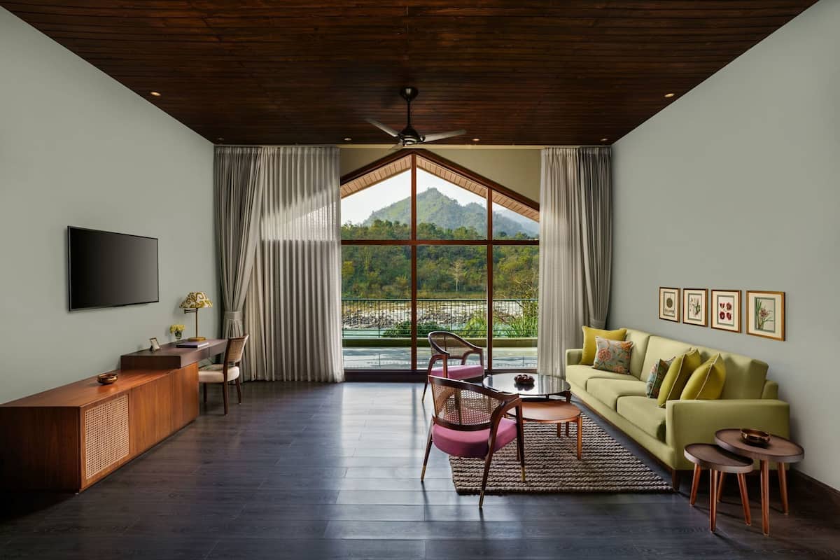 A spacious room with a wooden ceiling, a large window with curtains, a flat-screen TV, a sofa, and a dining area.