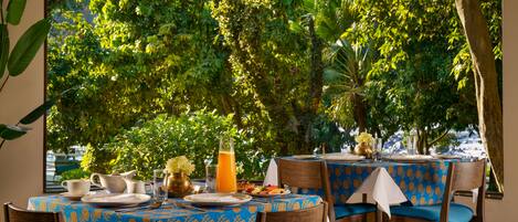 A dining area with tables set for breakfast, surrounded by lush greenery.