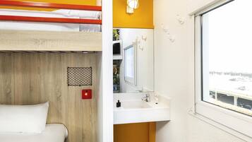 A bunk bed with a wooden panel design, a white sink with a mirror above it, and a window with a view of a parking area.