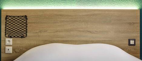 Una habitación ordenada con un cabecero de madera, una cama blanca y un objeto de malla negra en la pared.